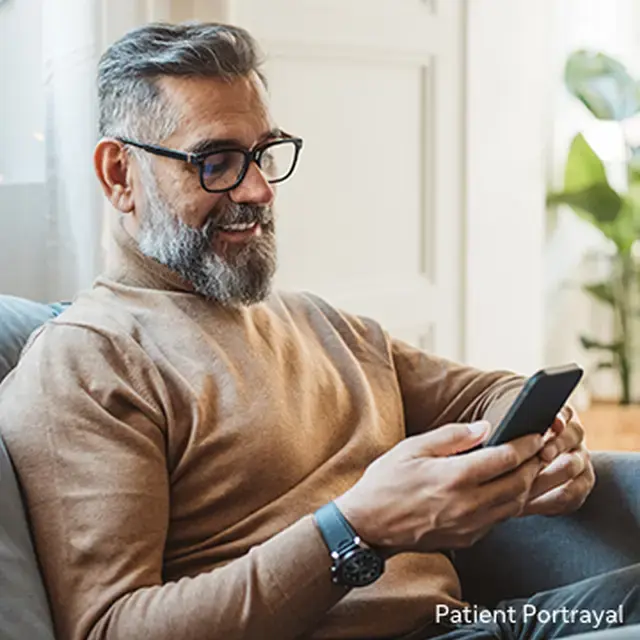 Patient portrayal of a man smiling and looking at a phone sitting on a couch