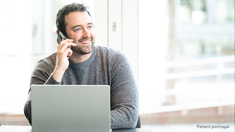 Patient portrayal of a man sitting at a desk with a laptop computer talking on a mobile phone