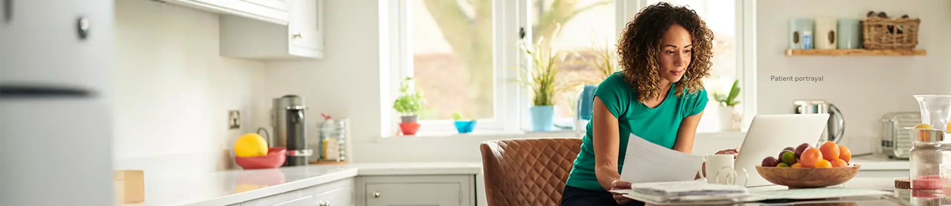 Patient portrayal of a woman sitting at a kitchen counter looking at a laptop computer